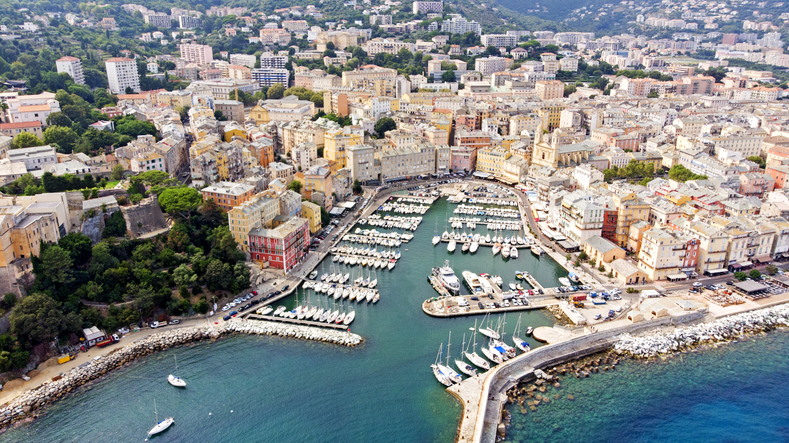 Ein weiter Blick aus der Luft auf den alten Hafen von Bastia mit zahlreichen kleinen Booten und der dichten Stadtbebauung.