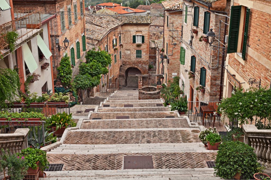 Eine lange, steile Steintreppe in einer historischen Gasse von Ancona, gesäumt von Ziegelhäusern und Pflanzen.