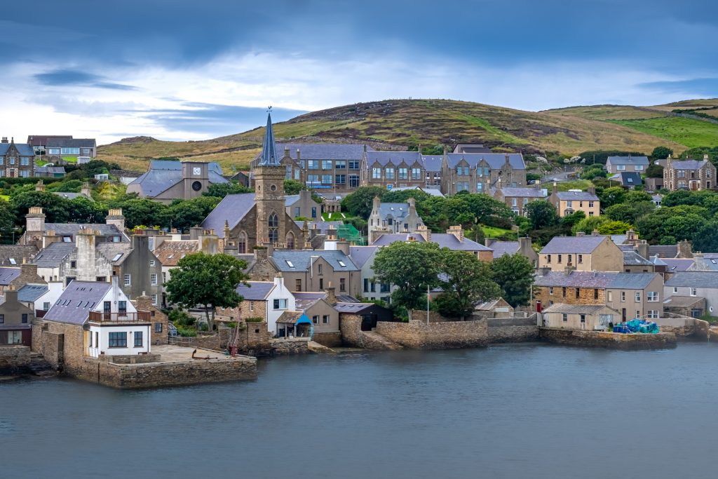 Blick auf ein charmantes Dorf an der Küste mit einer markanten Steinkirche und traditionellen Häusern am Wasser.