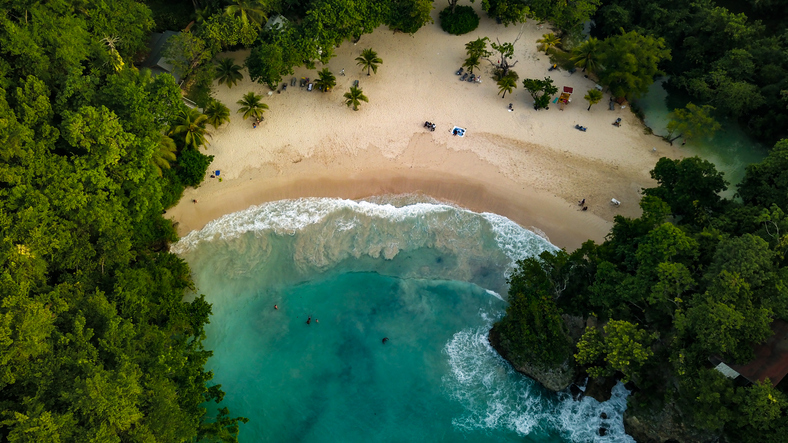 Ein Blick aus der Höhe zeigt eine geschwungene Bucht mit hellem Sand, umgeben von dichtem Regenwald und klarem Wasser.