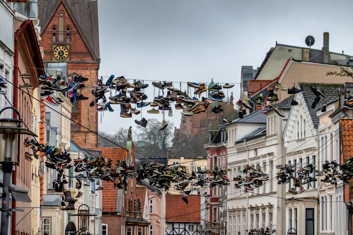 Über einer historischen Gasse mit Backsteingebäuden hängen zahlreiche Paare alter Schuhe an den Stromleitungen.