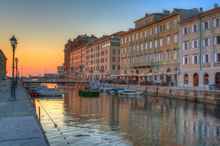 Restaurants mit Außenbestuhlung entlang einer Häuserfront am Kanal, während die Abendsonne den Himmel in warme Farben taucht.