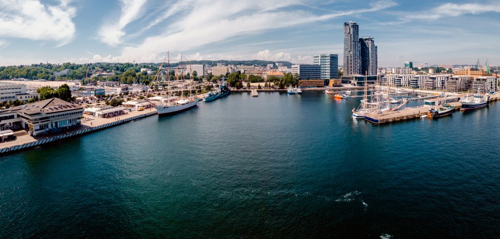 Eine weitwinklige Aufnahme des Hafens von Gdynia mit zahlreichen Schiffen, Kränen und der charakteristischen modernen Skyline im Hintergrund.
