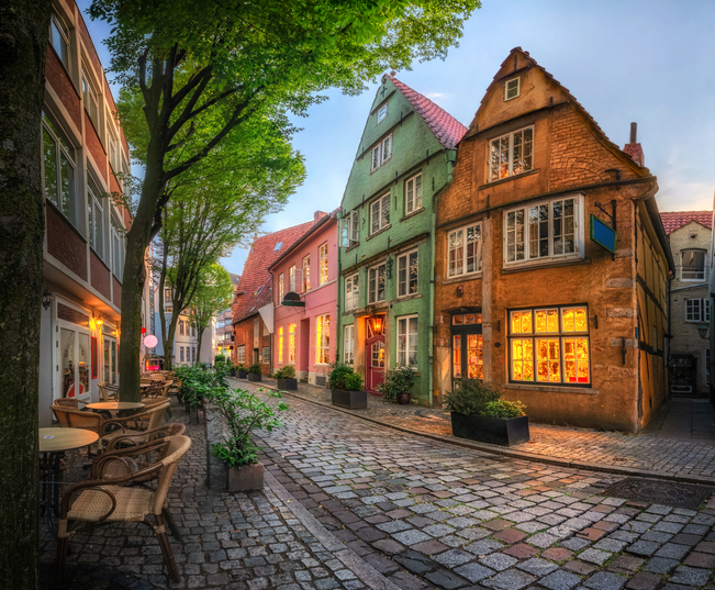 Eine ruhige, mit Kopfsteinpflaster belegte Straße mit bunten Häusern und stimmungsvoller Beleuchtung in den Fenstern.