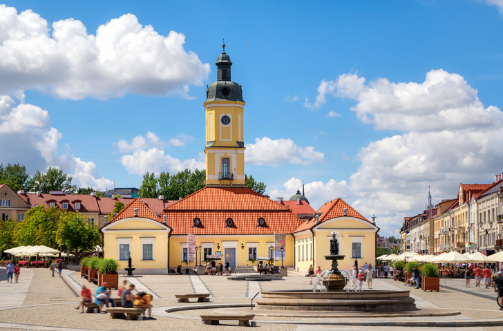 Der historische Marktplatz von Białystok mit dem markanten Rathaus und einem Brunnen bei strahlendem Sonnenschein.