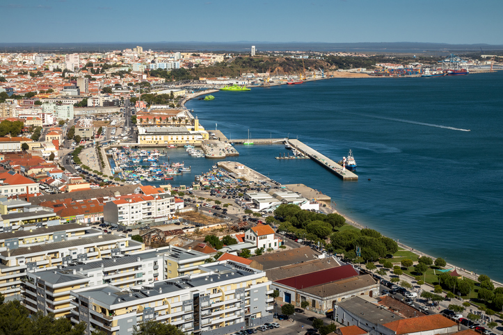 Eine weite Luftaufnahme der Küstenlinie von Setúbal mit dem belebten Hafenbecken, Fischerbooten und der angrenzenden städtischen Bebauung