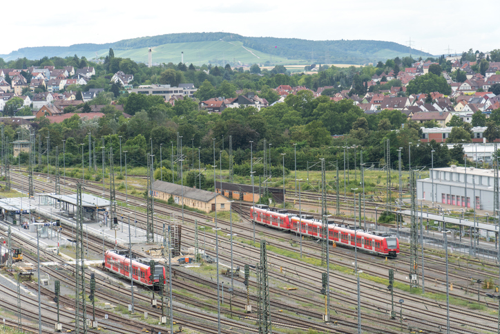 Rote Regionalzüge stehen an einem weitläufigen Gleisfeld vor der Kulisse der Stadt Heilbronn mit ihren grünen Weinberghängen im Hintergrund.