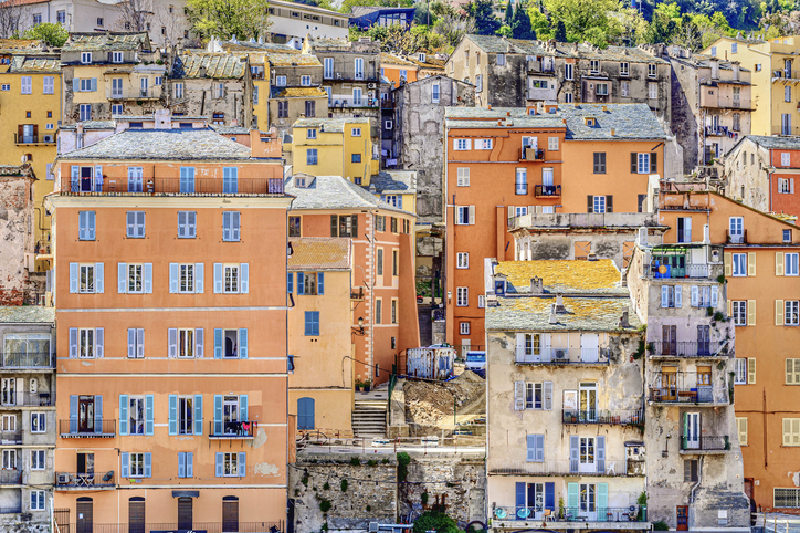 Eine Frontansicht der dicht aneinandergebauten, ocker- und orangefarbenen Häuser in Bastia mit blauen Fensterläden.