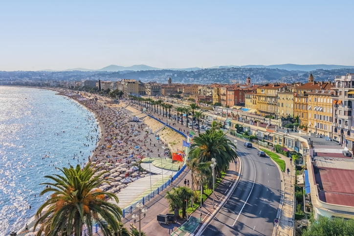 Die Strandpromenade von Nizza führt entlang der Bucht mit Palmen, Meer und Stadthäusern.
