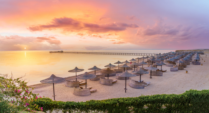 Leere Strandliegen und Sonnenschirme am Sandstrand von Hurghada unter einem dramatischen Abendhimmel.