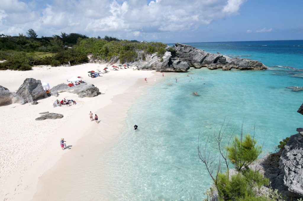 Ein feiner Sandstrand mit großen Felsen an der Seite grenzt an das durchsichtige, türkisblaue Meer.