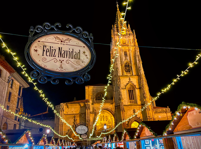 Die beleuchtete Kathedrale von Oviedo steht hinter festlichen Weihnachtsständen und Lichterketten.