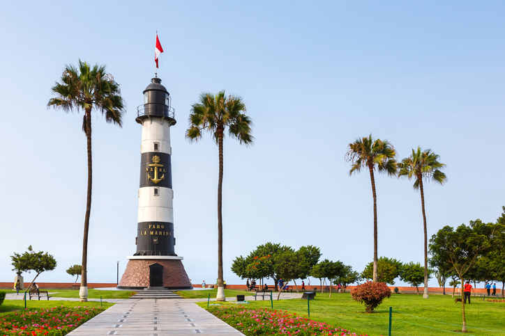 Der schwarz-weiß gestreifte Leuchtturm „Faro La Marina“ in Lima, umgeben von Palmen und gepflegten Grünflächen.