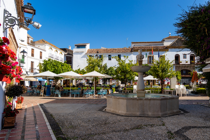 Der von Orangenbäumen gesäumte Plaza de los Naranjos in Marbella mit einem historischen Brunnen in der Mitte und Tischen von umliegenden Cafés.