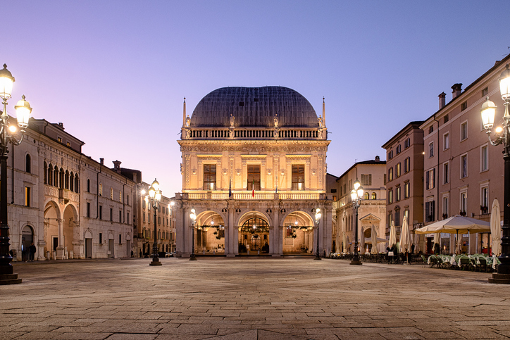 Der beleuchtete Platz Piazza della Loggia in der Abenddämmerung mit den warmen Lichtern der umliegenden Gebäude.