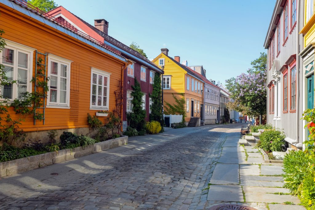 Eine ruhige Straße mit Kopfsteinpflaster, gesäumt von farbenfrohen, traditionellen norwegischen Holzhäusern.