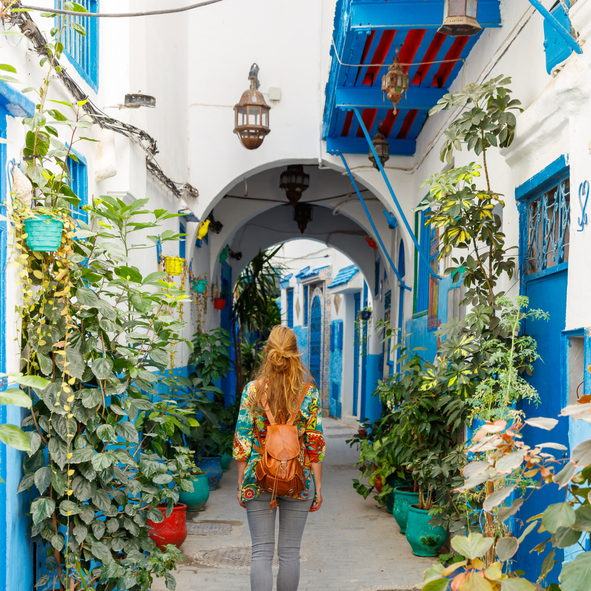 Eine Reisende läuft durch eine weiß-blaue Gasse mit Pflanzen und traditionellen Häusern nahe Tanger.