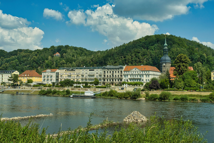 Historische Gebäude und grüne Hügel liegen am Ufer der Elbe in der Sächsischen Schweiz.
