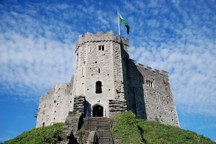 Die steinernen Mauern von Cardiff Castle erheben sich auf einem Hügel unter blauem Himmel.