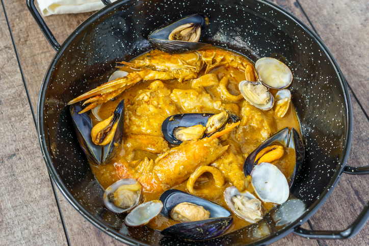 Eine gusseiserne Pfanne mit einer köstlichen Meeresfrüchte-Mischung, darunter Garnelen, Muscheln und Tintenfisch in einer kräftigen Soße.