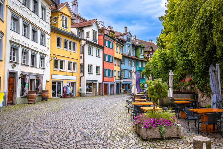 Eine pittoreske Gasse mit farbenfrohen Gebäuden, die durch Blumenkästen und einladende Außenbestuhlung der Gastronomie geschmückt ist