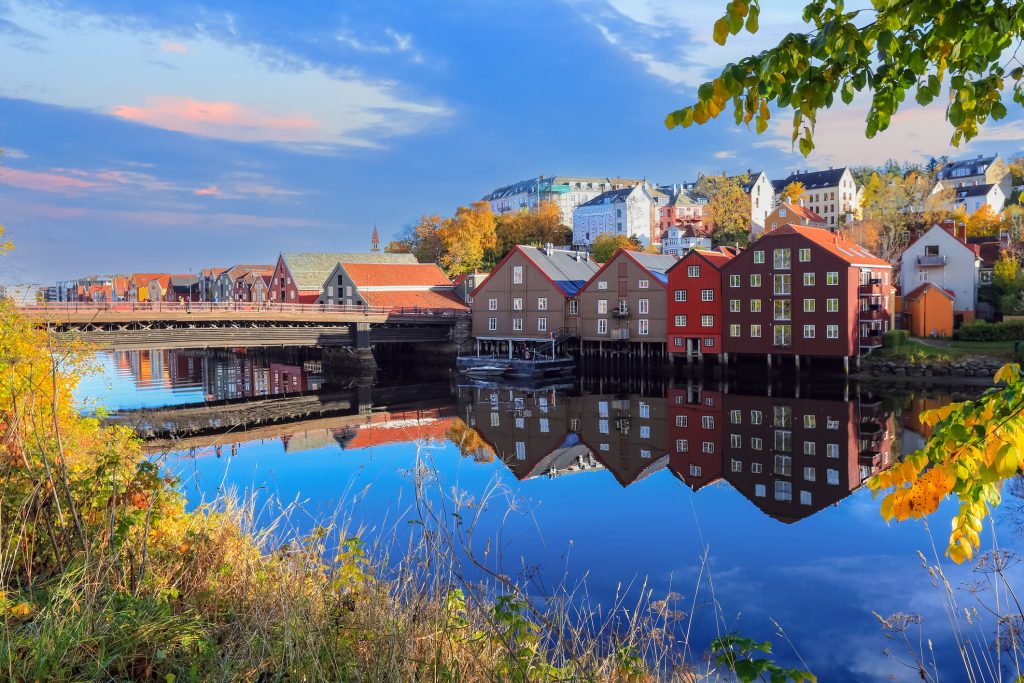 Die charakteristischen roten und braunen Speicherhäuser spiegeln sich im ruhigen Wasser des Nidelva-Flusses.