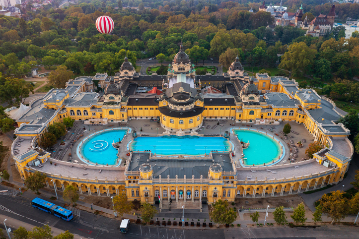 Luftaufnahme des großen Széchenyi-Heilbads mit gelbem Gebäude und türkisfarbenen Becken in Budapest.