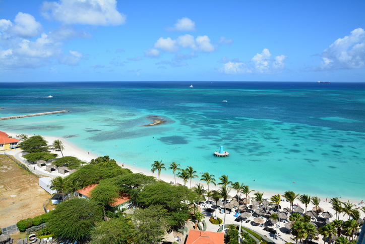 Türkisblaues Meer, heller Sandstrand und Palmen zeigen die karibische Küste von Aruba.