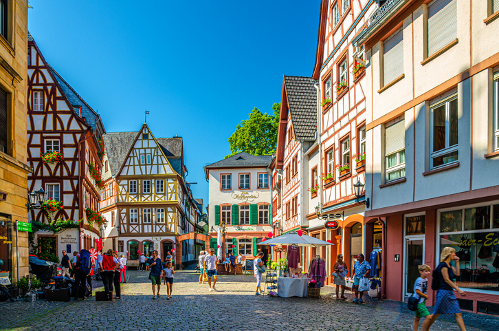 Ein idyllischer Platz in der Mainzer Altstadt mit traditionellen Fachwerkhäusern und Kopfsteinpflaster, auf dem sich Menschen bei Sonnenschein aufhalten.