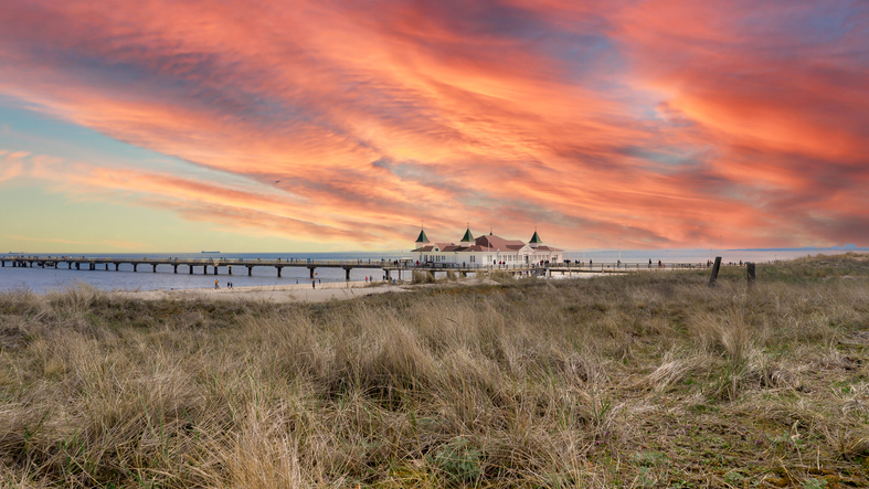 Die Seebrücke von Ahlbeck erstreckt sich in das Meer unter einem dramatischen, orange gefärbten Abendhimmel.