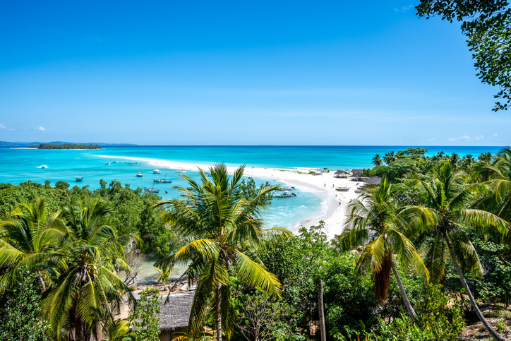 Der Blick von Palmen aus auf eine malerische Bucht mit weißen Sandbänken und strahlend blauem Wasser in Madagaskar.
