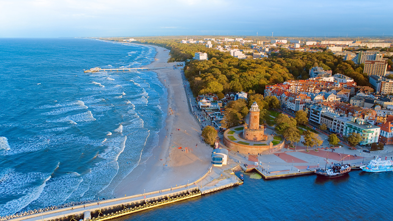 Ein weitläufiger Luftbildblick zeigt die Hafeneinfahrt, den Leuchtturm und den kilometerlangen Sandstrand der Stadt Kolberg.