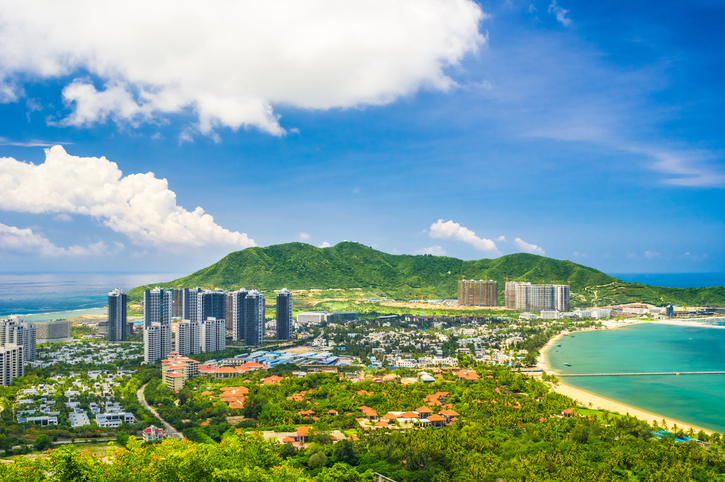 Ein hoher Blick auf eine grüne Hügellandschaft, die sanft zu einer türkisfarbenen Bucht und Sandstränden auf Hainan abfällt.