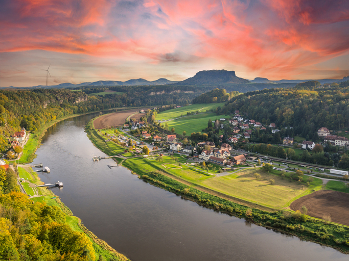 Die Elbe schlängelt sich durch grüne Landschaft und Felsen der Sächsischen Schweiz.