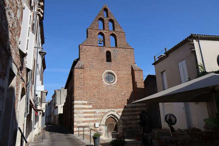 Die Frontansicht einer Kirche aus rotem Backstein in einer ruhigen Gasse von Agen.