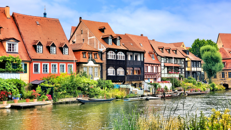 Eine Reihe von charmanten Fachwerkhäusern mit roten Dächern säumt das Ufer des Flusses Regnitz.