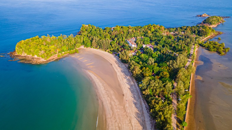Eine grüne, bewaldete Landzunge ragt in das türkisfarbene Wasser, gesäumt von einem feinen Sandstrand.