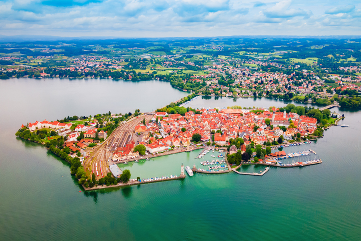 Eine beeindruckende Drohnenaufnahme zeigt die gesamte Insel mit dem Bahnhof, der dichten Bebauung und der Hafeneinfahrt umgeben vom türkisblauen See