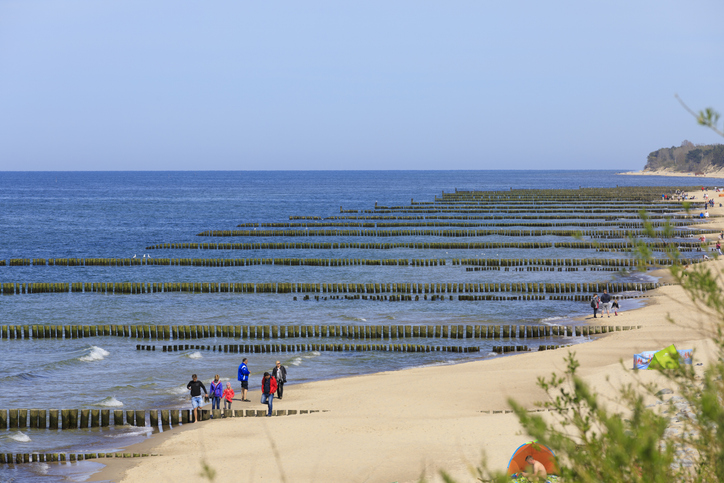 Lange Reihen von hölzernen Wellenbrechern erstrecken sich bei Sonnenschein tief in die Ostsee vor dem breiten Sandstrand von Kolberg.