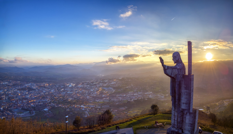 Eine große Christusstatue blickt bei Sonnenuntergang vom Monte Naranco auf Oviedo.