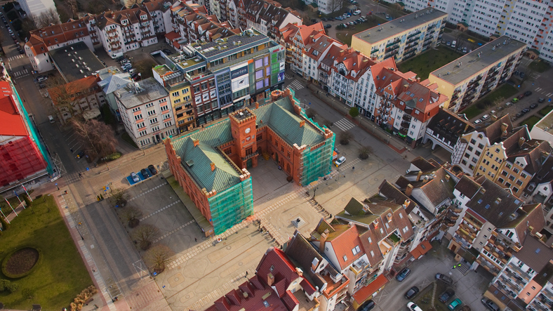 Ein hoher Blick auf den historischen Marktplatz und die Gebäude im Zentrum von Kolberg, die teilweise von Baugerüsten umgeben sind.