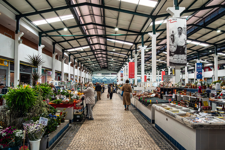 Eine helle, geräumige Markthalle mit hohen Decken und Menschen, die durch die Gänge zwischen den Verkaufsständen schlendern