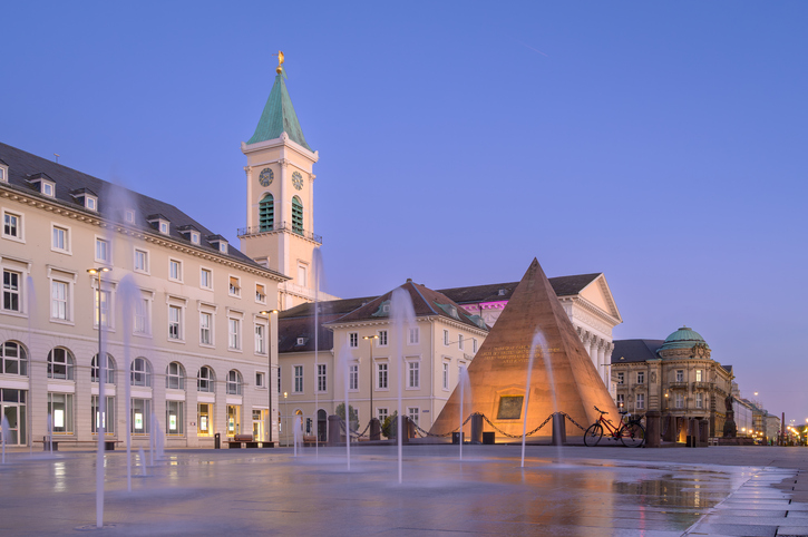 Die berühmte Pyramide auf dem Marktplatz von Karlsruhe vor der beleuchteten Kirche bei Sonnenuntergang.