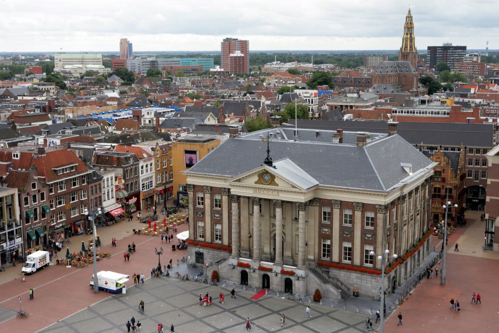 Eine Luftaufnahme zeigt das beeindruckende Rathaus am belebten Grote Markt in Groningen, im Hintergrund ist der Martiniturm sichtbar.