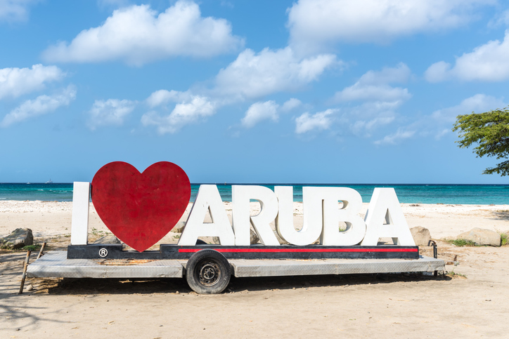 Das bekannte I Love Aruba Schild steht direkt am Strand vor türkisblauem Meer.