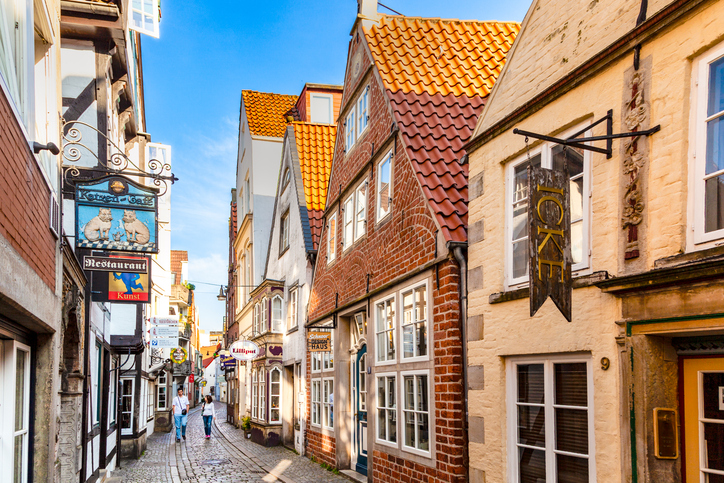 Eine schmale, gepflasterte Gasse mit historischen Backsteinhäusern, die von hübschen Schildern und Lampen geschmückt ist.