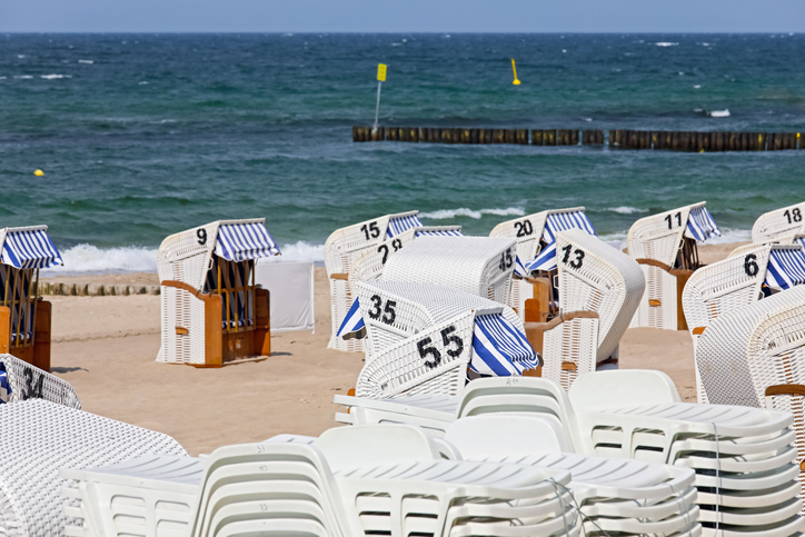 Weiße Strandkörbe stehen in Reih und Glied am feinen Sandstrand von Kolberg, im Hintergrund glitzert das blaue Wasser der Ostsee.