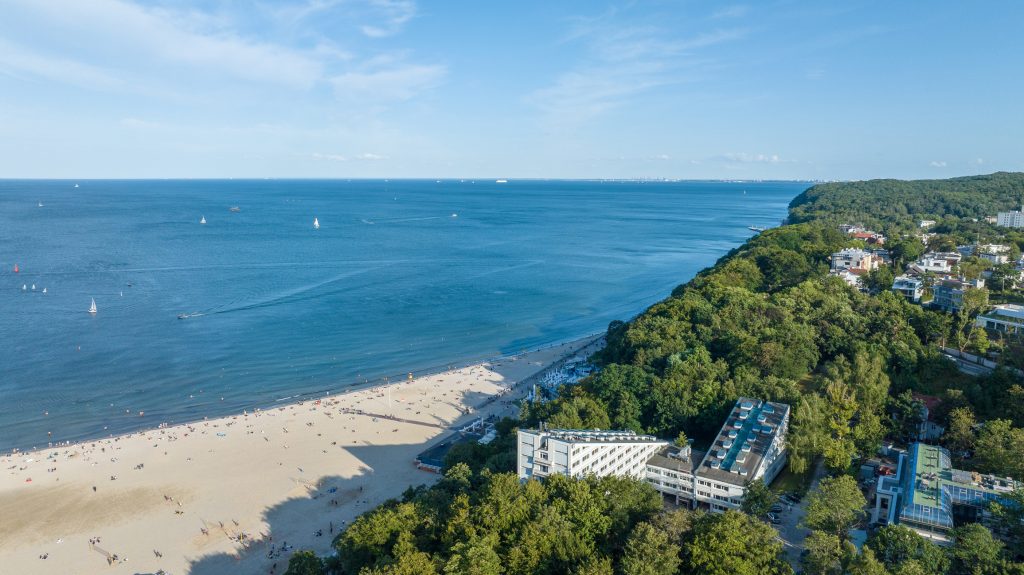 Eine Drohnenaufnahme zeigt den Sandstrand von Gdynia, das angrenzende Waldgebiet und den Blick über die endlose Ostsee.
