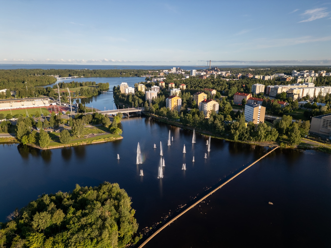 Ein großer Fluss mit zahlreichen Wasserfontänen, die in die Höhe schießen, vor einer grünen Stadtkulisse.