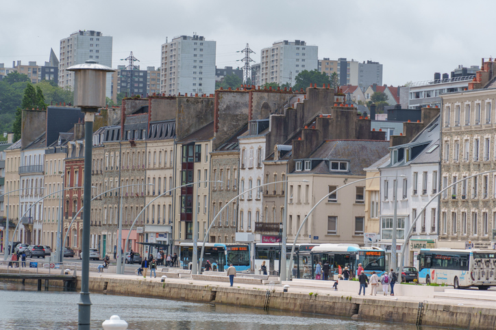 Eine Uferpromenade in Cherbourg mit Bussen, Fußgängern und den typischen alten Häuserfassaden im Hintergrund.